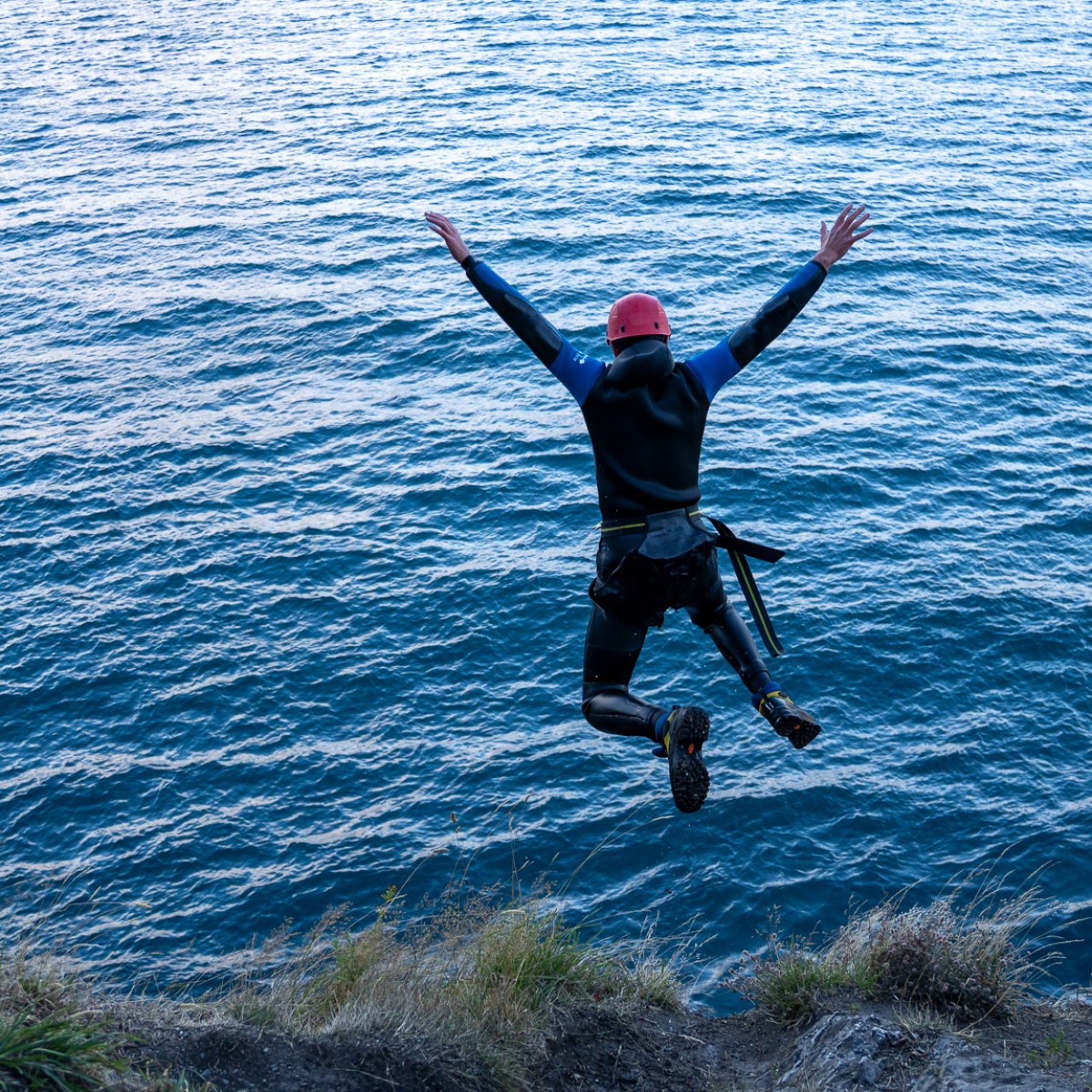 Person in wetsuit jumping into the ocean from a cliff.