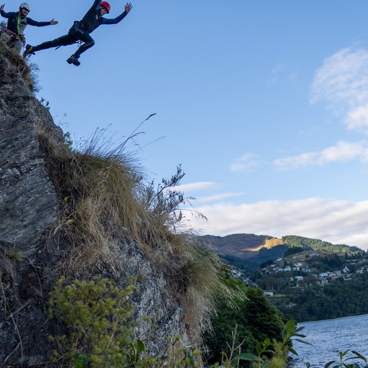 Person in wetsuit jumping off rock into lake, surrounded by trees.