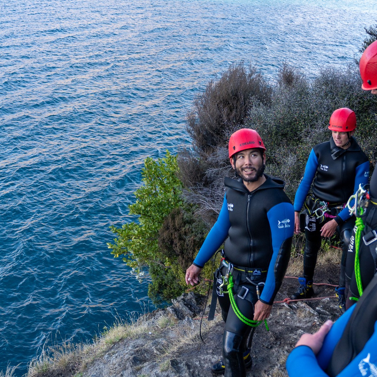 Group of climbers in gear and helmets by a water body.