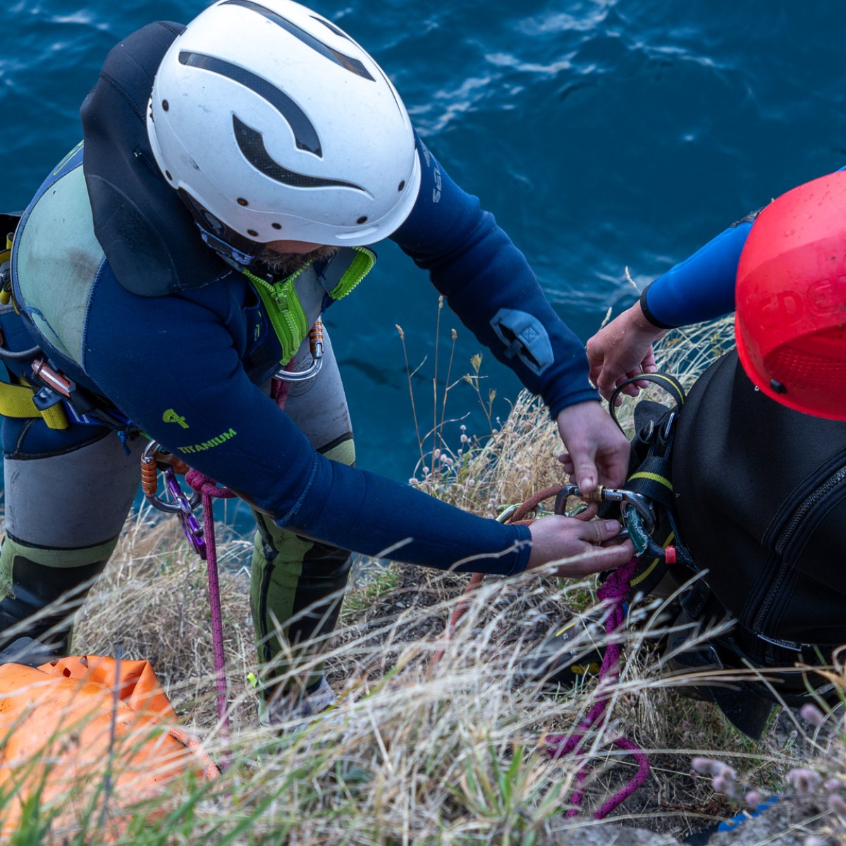 Two climbers on a cliffside securing ropes above water.